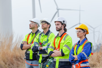 Teamwork engineer wearing safety uniform standing crossed arms at wind turbine field renewable...