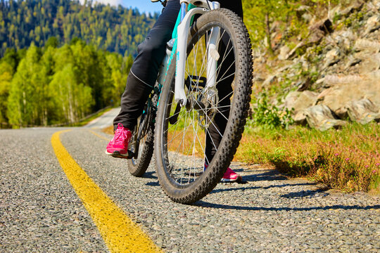 Close-up of part of the bike and cyclist. stopped on the side of the road on a highway in a hilly area. Girl athlete on a mountain bike stopped for a rest on road or starts moving to meet adventures