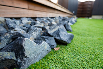 木製のウッドデッキの縁側の下に敷き詰められた中サイズの綺麗な石、岩と青々と茂っている芝生