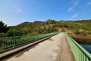 Fototapeta na wymiar paisaje de montaña con lago y pasarela con barandilla de hierro verde en Marbella España