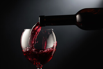 Pouring red wine into a wine glass. - obrazy, fototapety, plakaty
