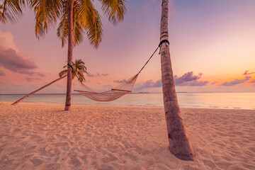 Beautiful silhouette of hammock on palm trees on tropical beach paradise at sunset. Carefree...