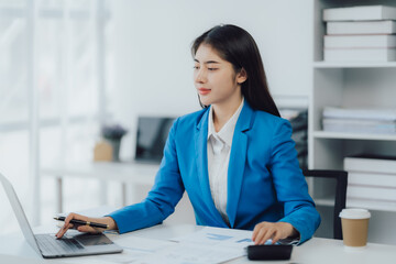 Asian Business woman using calculator and laptop for doing math finance on an office desk, tax, report, accounting, statistics, and analytical research concept