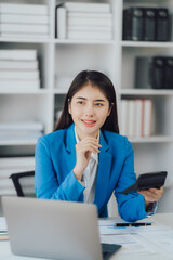 Asian Business woman using calculator and laptop for doing math finance on an office desk, tax, report, accounting, statistics, and analytical research concept