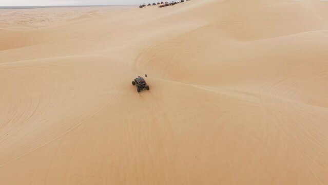 Aerial view of ATV buggy sport car riding by sand dunes. Extreme sport outdoor hobby activity for weekend day. Sport recreation concept for male. Group of four wheel drive vehicles competing on dunes