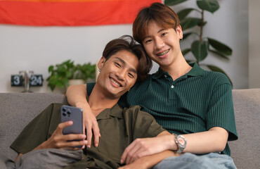 Happy homosexual couple relaxing on couch at home, spending time together at home. LGBT, love, relationship and equality concept.