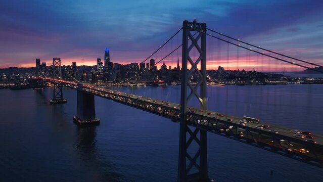 Aerial view of San Francisco Oakland Bay Bridge full of night traffic. Financial district skyline in the background at dramatic colorful sunset sky. Cinematic panorama of San Francisco, California USA