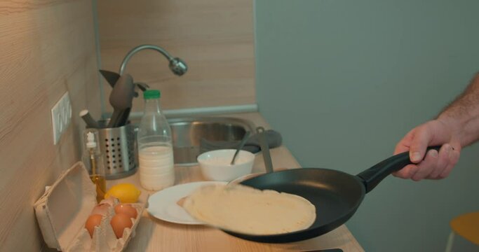 Man holds pan, flips a pancake in the kitchen. guy has fun with your food. Shot of a young man making pancakes at home. close up side view cropped video slow motion