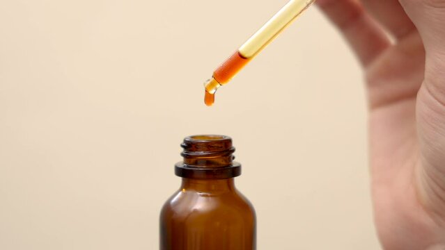 woman applying on face finger vitamin c serum pink color liquid.face care anti wrinkle acne aging procedures.young female applying with finger on cheek. 4k. drops falling from pipette