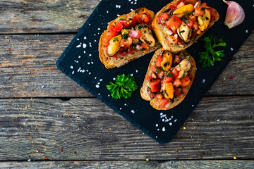 Tasty sandwiches - toasted bread with tomatoes and mussels on wooden table
