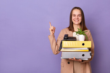 Joyful woman office worker with cardboard box with her things has new job pointing at copy space...