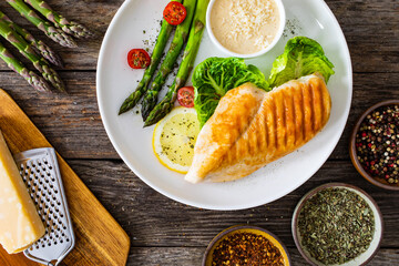 Barbecued chicken breast and green asparagus on wooden table
