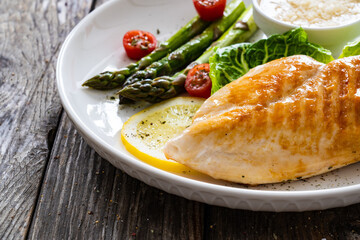 Barbecued chicken breast and green asparagus on wooden table
