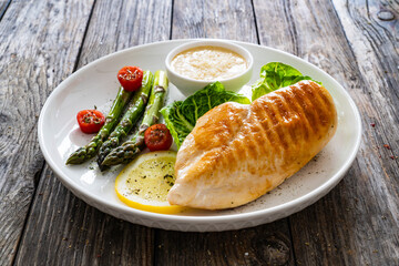 Barbecued chicken breast and green asparagus on wooden table
