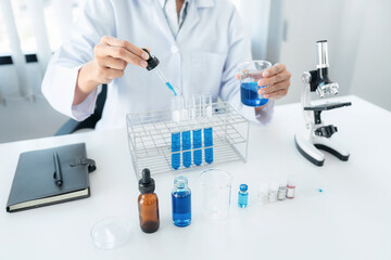 Scientist woman holding beaker and dropper to dropping blue liqu