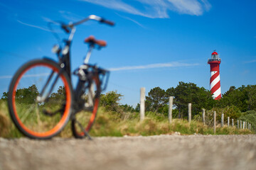 Dutch lighthouse red white against blue sky. Comfort bicycle out of focus on stony path. Sunny summer afternoon. Netherlands, Zeeland, Haamstede.