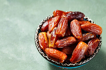Pitted sweet dates on a green background. Bowl of dried dates for Ramadan. Copy space. Top view