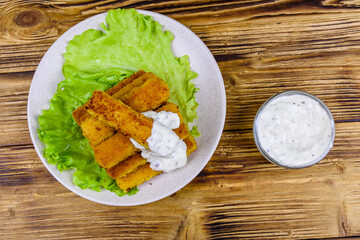 Baked fish sticks and lettuce leaves in a plate. Top view