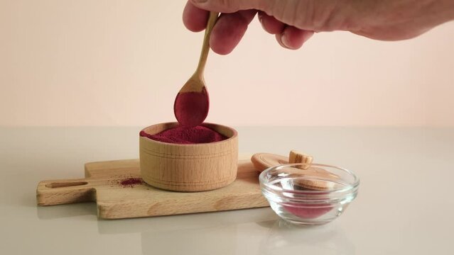 Man's hand picks up dry beetroot powder with wooden spoon to make vegan smoothie or beetroot latte drink. Food additive E162, natural pigment beet red. Superfood, antioxidant.
