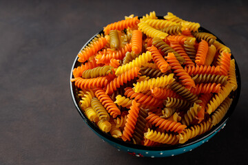 Fusilli dry pasta on a dark background. Tricolor fusilli pasta in a bowl. Top view. Copy space