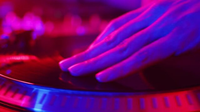 DJ chooses the right places for mixing by hands on the record with high accuracy, which rotates on the turntable during the studio recording of the vinyl session in a color light close up