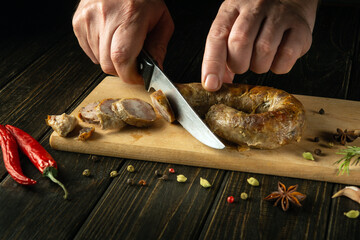 The hands of the cook with a knife cut grilled pork sausage on a cutting kitchen board for a delicious lunch. Northern Thailand national dish