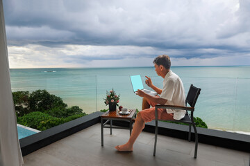 Senior digital nomad man working at luxury villa in Phuket. andaman sea as background.