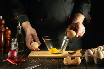 Eggs in the cook hands before breaking into a bowl. Cooking scrambled eggs for lunch in the restaurant kitchen. Egg diet concept