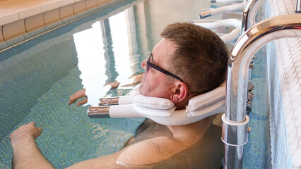 The procedure of underwater traction of the spine in the pool. A man hangs in the water, with...