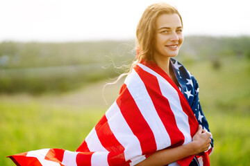 Young woman waves an american flag on blooming meadow. 4th of July. Independence Day. Patriotic holiday. 