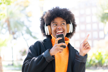 African American girl at outdoors listening music with a mobile and singing