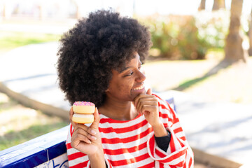 African American girl holding a donut at outdoors thinking an idea and looking side