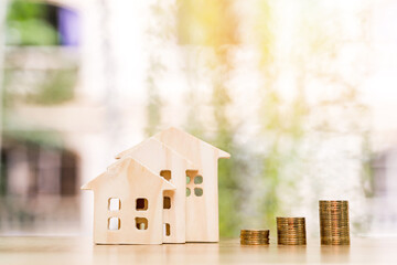 Wooden house model and stack gold coin of sunlight in the public park, Saving money or loan for business investment real estate or buy a new home for a family concept.