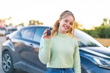 Fototapeten Young pretty girl holding car keys at outdoors smiling a lot © luismolinero