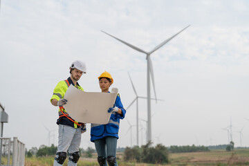 Male and female engineer in uniform with helmet safety holding blueprint and discussing to inspection and maintenance of wind turbine in wind farm to generate electrical energy, Renewable power energy © Supachai