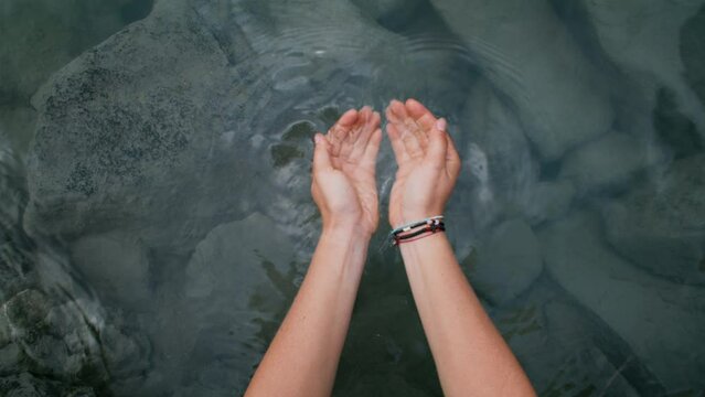 POV of female hands scoop clear water into palms of her hands. Holistic and environment conscious lifestyle concept. Conservation of natural resources. Clear and clean water in nature