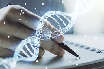 Double exposure of creative DNA hologram and man hand writing in notebook on background. Bio...