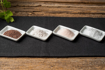 Small bowls with different types of salt, black, pink, flake and seasoned with truffle, on a tablecloth on a rustic table.