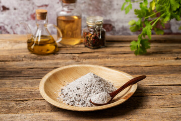 Wooden plate with truffle seasoned salt, on a rustic wooden table with jars of pepper, vinegar and olive oil, close-up.