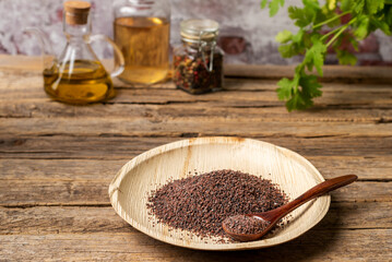 Wooden plate with Himalayan black salt, on a rustic wooden table with jars of pepper, vinegar and olive oil, close-up.