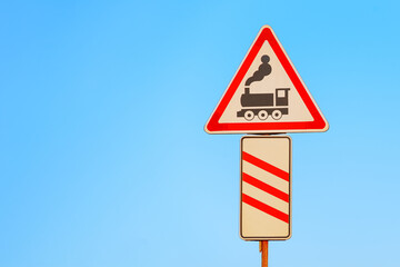Level crossing warning sign on blue sky background. Railway transportation safety symbol.