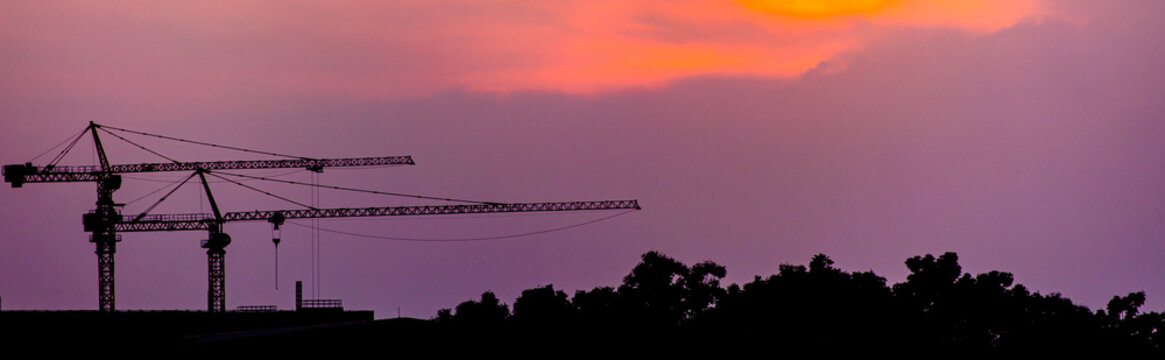 A blue slan surrounds the building under construction. Crane. Crane for lifting things in construction against sunset sky atmosphere. communities and large industrial construction zones.	
