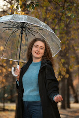 Portrait of happy smiling young woman with lush hair and under transparent umbrella. Student in autumn park