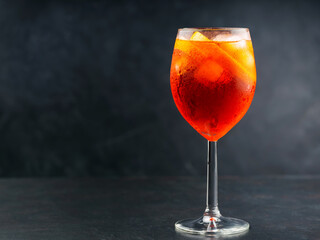Aperol Spritz cocktail in glass with fresh orange on dark background. Glass of ice cold Aperol Spritz cocktail served in a wine glass. Copy space
