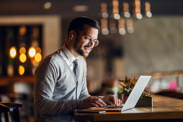 A young focused businessman in smart casual is typing on the laptop and working remotely from cafe.