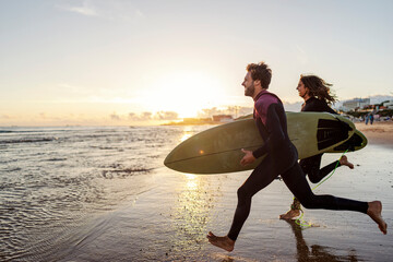 An excited couple rushing into the water with surfboards.