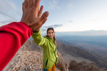 A woman with a backpack climbed to the top of the mountain and gives a high five..
