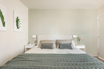 Stylish bright bedroom with bedside tables and a double bed with green beige wallpaper and cute pictures on the wall. The concept of a small but cozy and multifunctional apartment. Copyspace