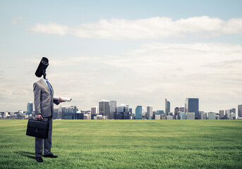 Camera headed man standing on green grass against modern cityscape