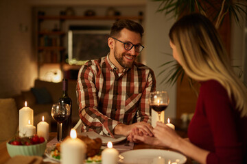 Beautiful couple having romantic dinner with candles and red wine at home